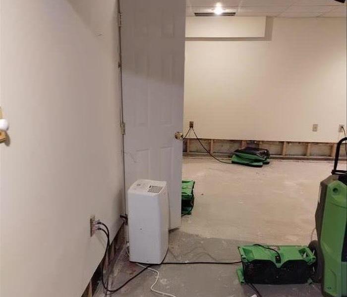 A room with the dry wall cut out of the bottom two feet of the wall with a fan going to dry up the water damaged area.